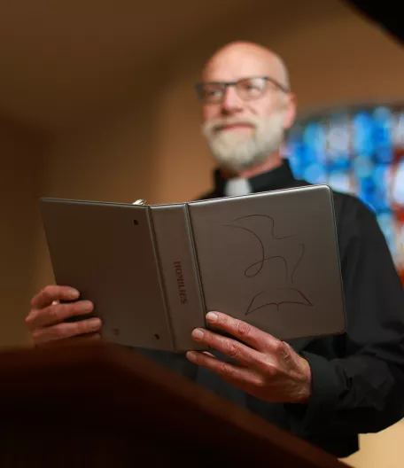 priest holding a gray binder 